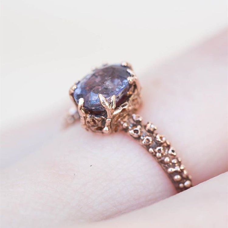 Rose gold ring with a large purple gemstone on a light background