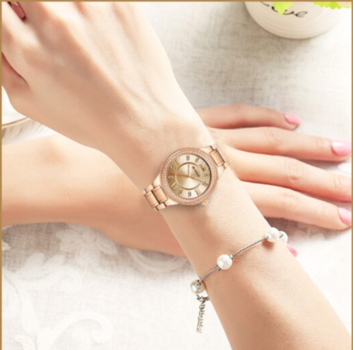 Rose gold watch on a wrist with a pearl bracelet against a soft background