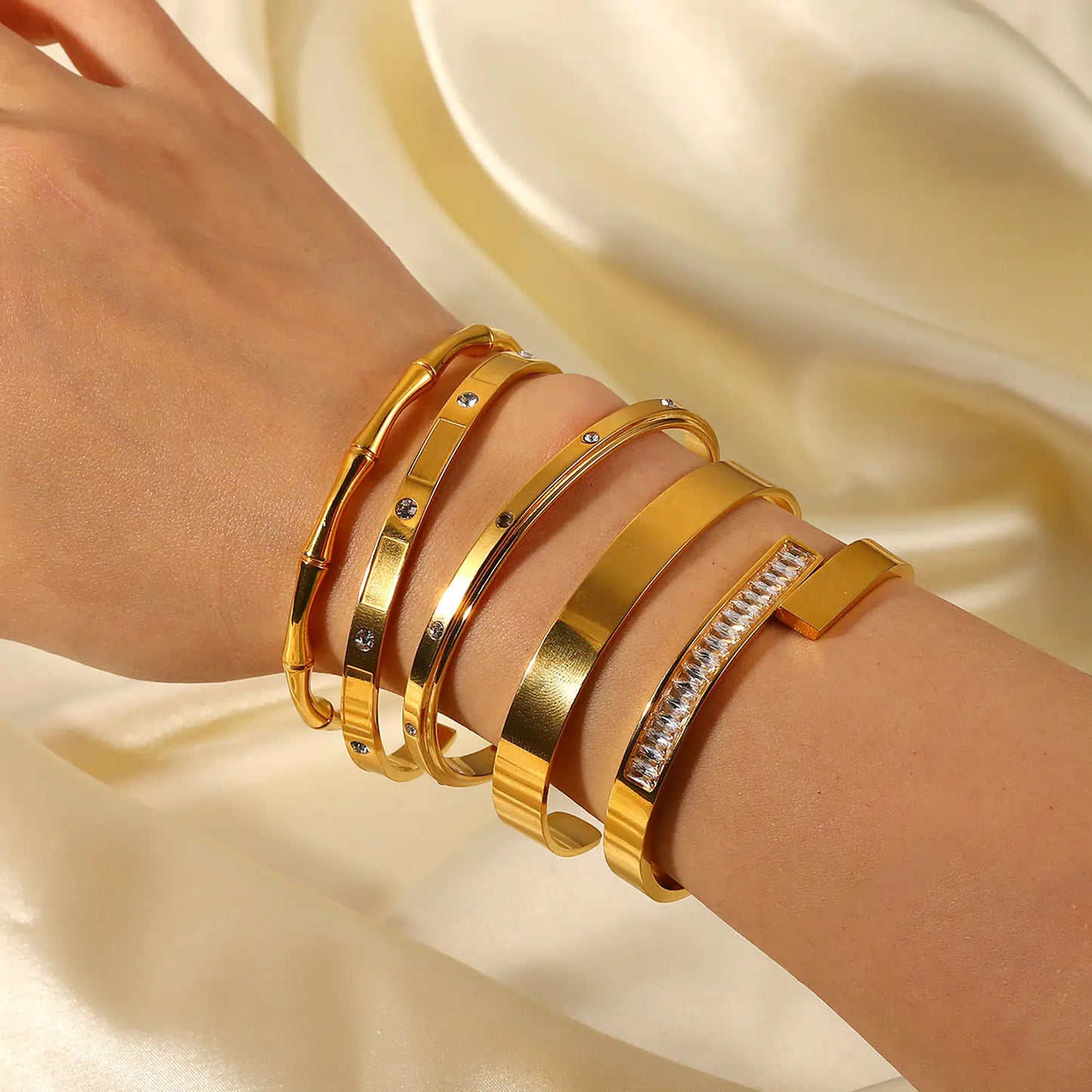 Gold bracelets on a wrist with a beige satin background