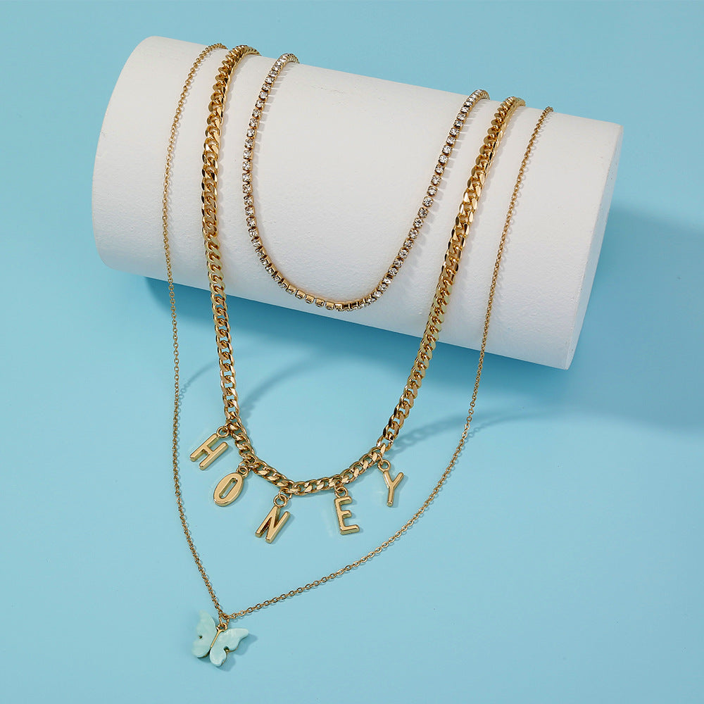 Gold necklaces with 'HONEY' pendant on a white cylindrical stand against a light blue background