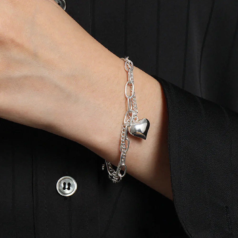 Silver bracelet with heart charm on a wrist against a black background