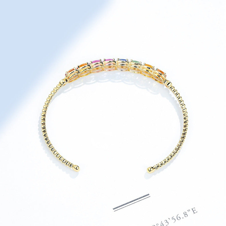 Gold bracelet with colorful stones on a light blue background