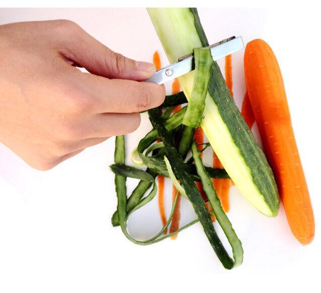 Hand using a vegetable peeler to strip zucchini and carrot on a white background
