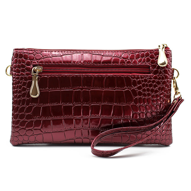 Maroon crocodile-patterned clutch bag with gold zippers on a white background