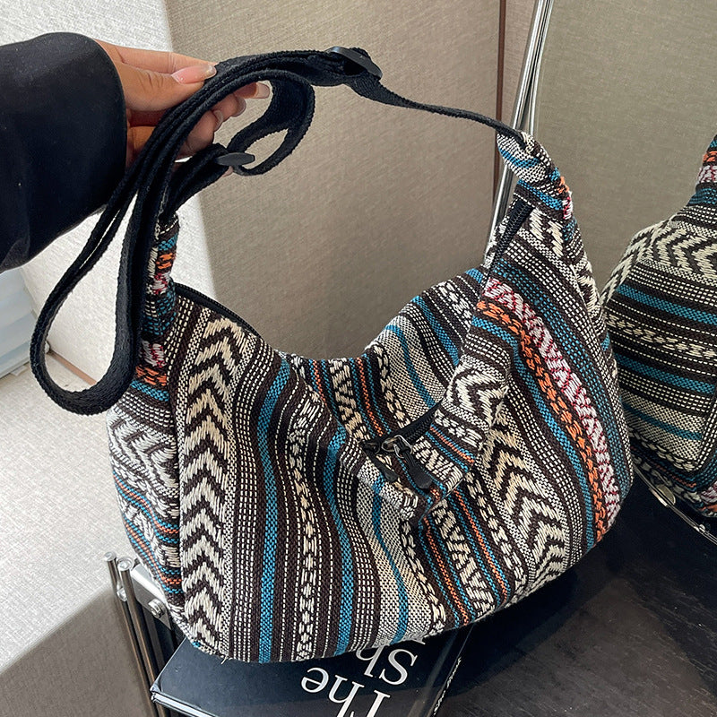 Patterned handbag with a black strap held by a person, with another similar bag in the background.