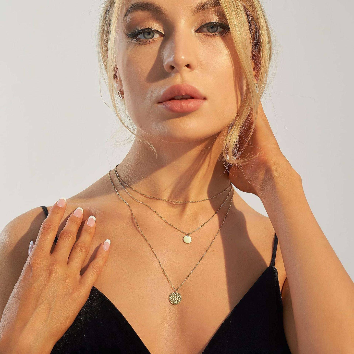 Woman wearing a black top and gold necklaces against a neutral background