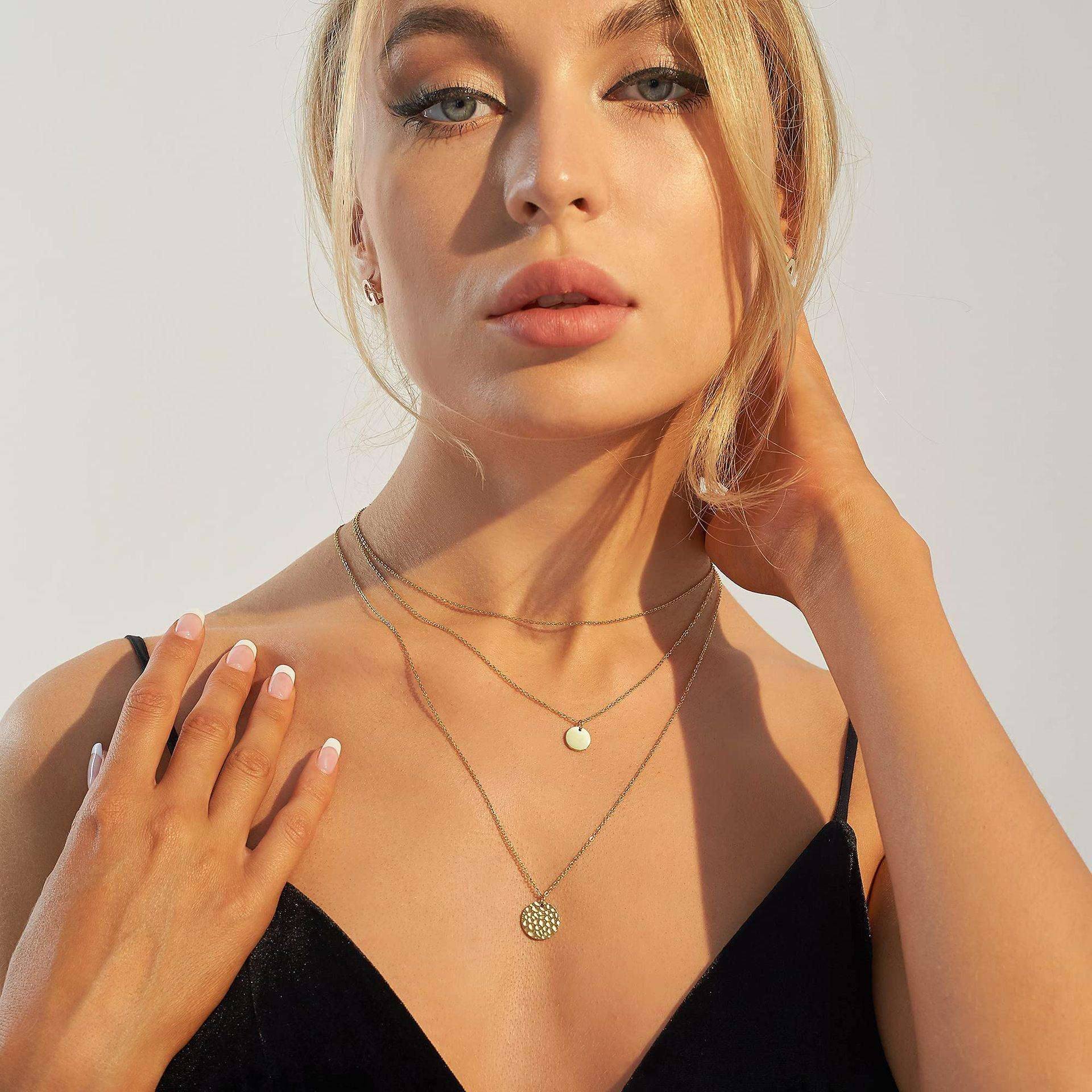 Woman wearing a black top and gold necklaces against a neutral background