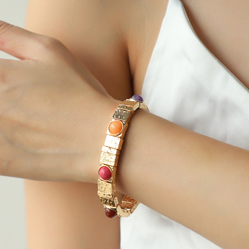 Gold bracelet with colorful beads on a wrist against a neutral background