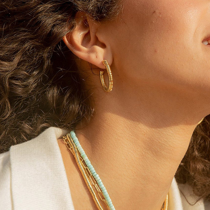 Close-up of a person wearing gold hoop earrings and necklaces.