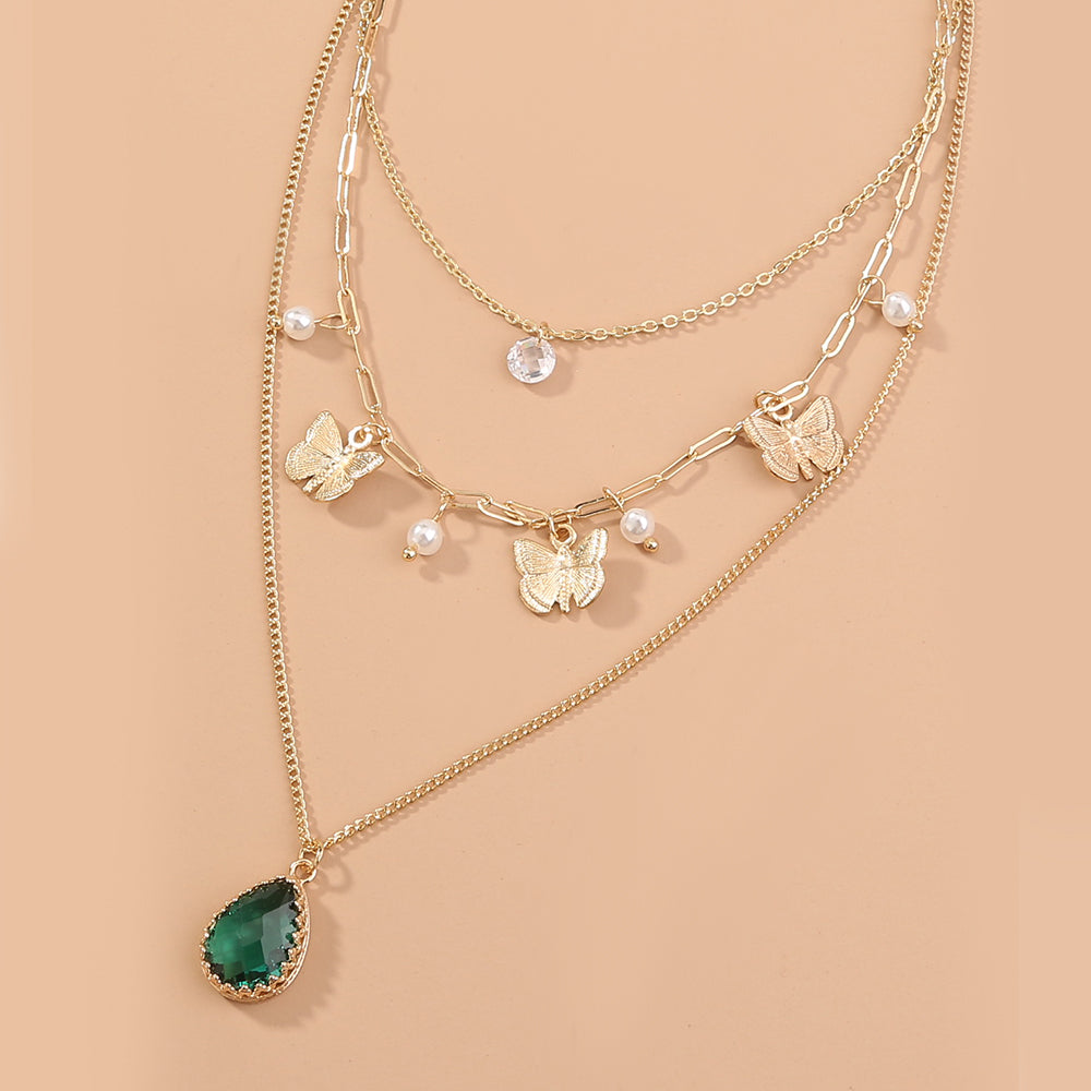 Layered gold necklaces with butterfly and green teardrop pendants on a beige background