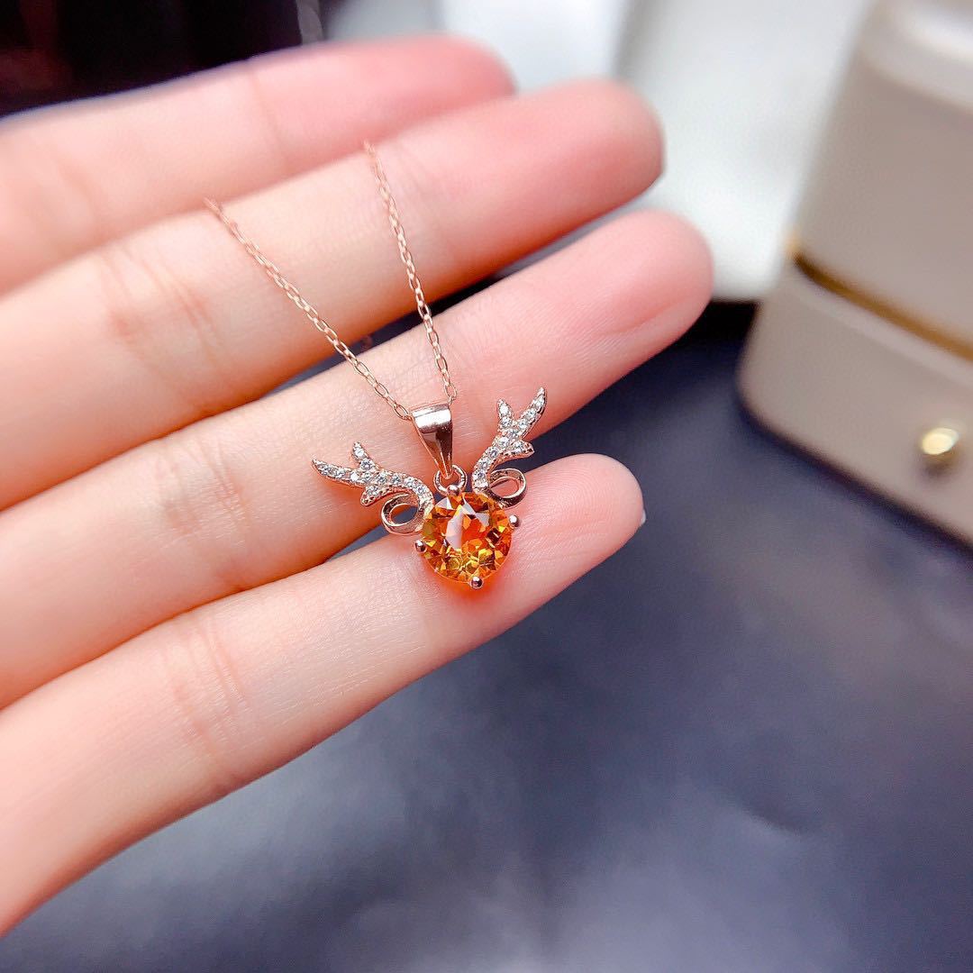 Heart-shaped orange gemstone pendant on a gold chain held in a hand.
