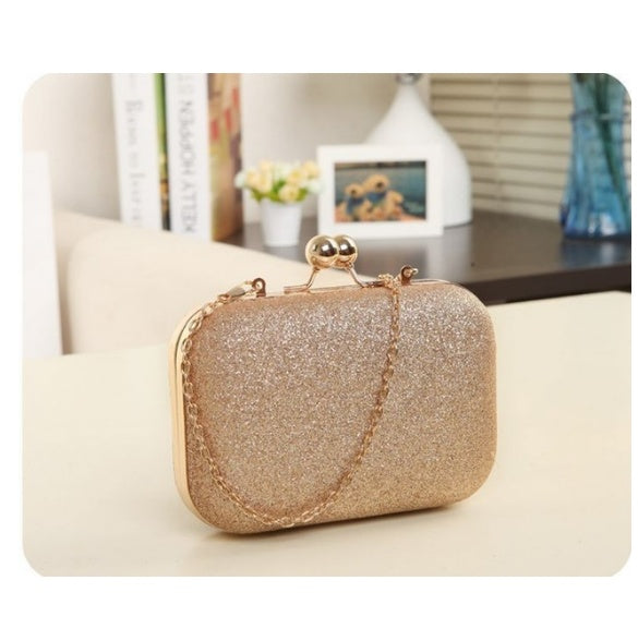 Gold glitter clutch bag on a light surface with a blurred background