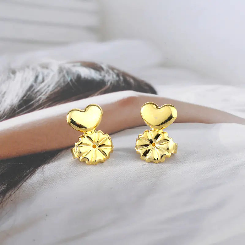 Gold heart-shaped earrings worn by a person on a blurred background
