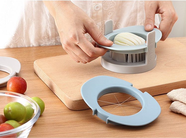Person using a kitchen tool to slice bread on a wooden cutting board with fruits and a bowl in the background.