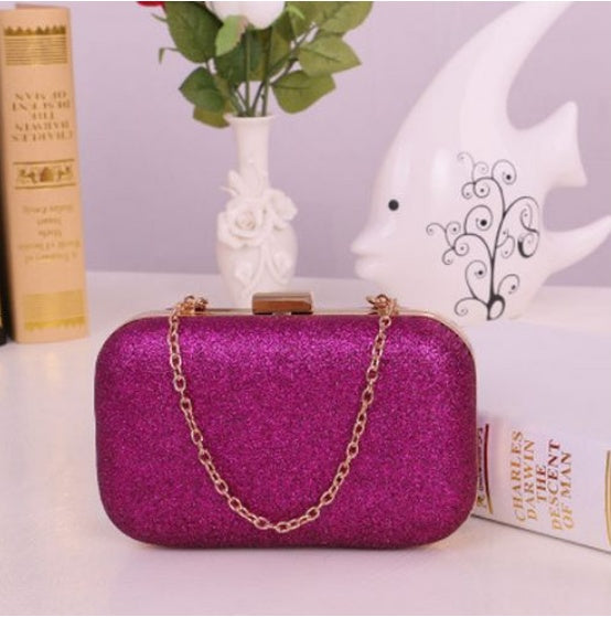 Purple glittery clutch bag with a gold chain on a surface with decorative items in the background.