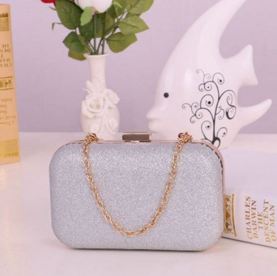 Silver glitter clutch bag with a gold chain on a white surface with decorative items.