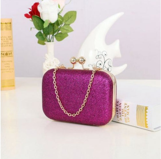 Purple glittery clutch bag with gold chain on a white surface with decorative items.