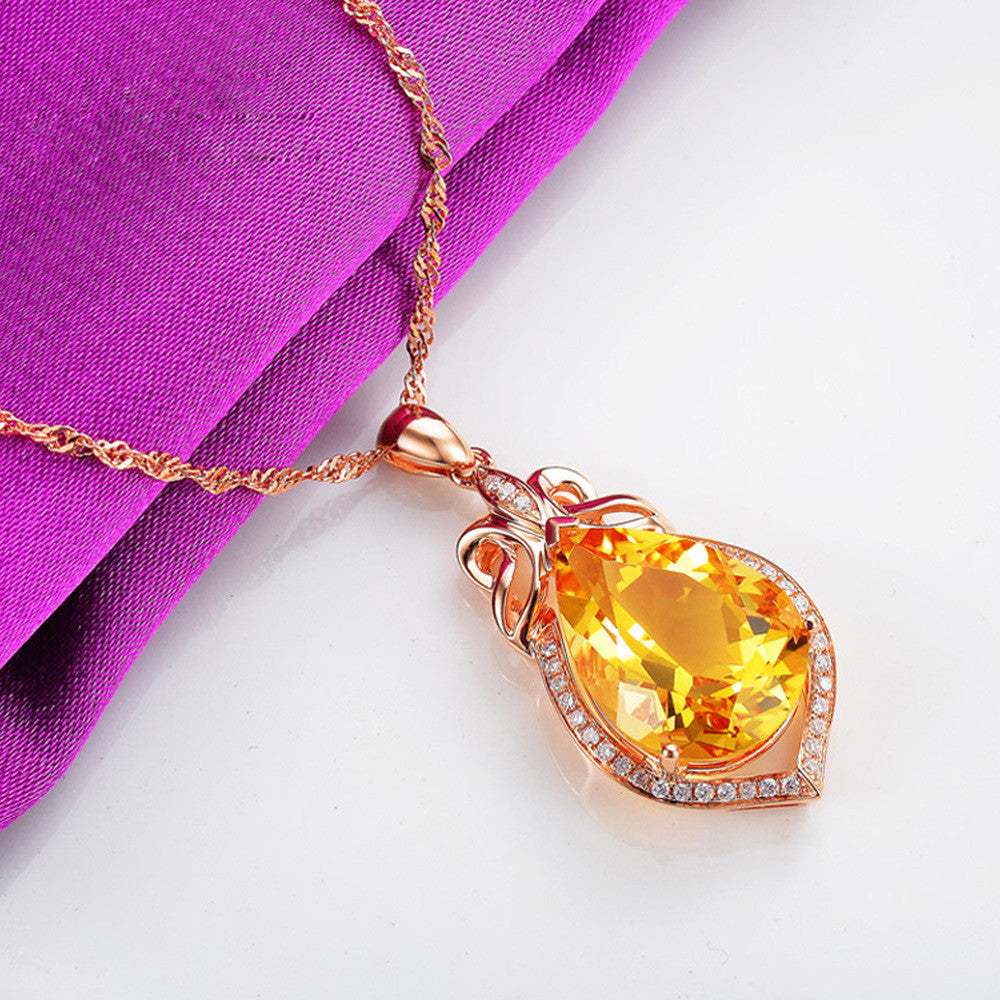 Gold necklace with a yellow teardrop-shaped gemstone pendant on a white background