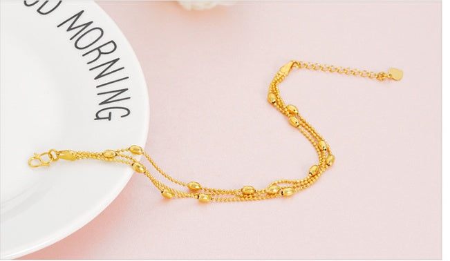 Gold anklet on a person's ankle with a 'Good Morning' card in the background