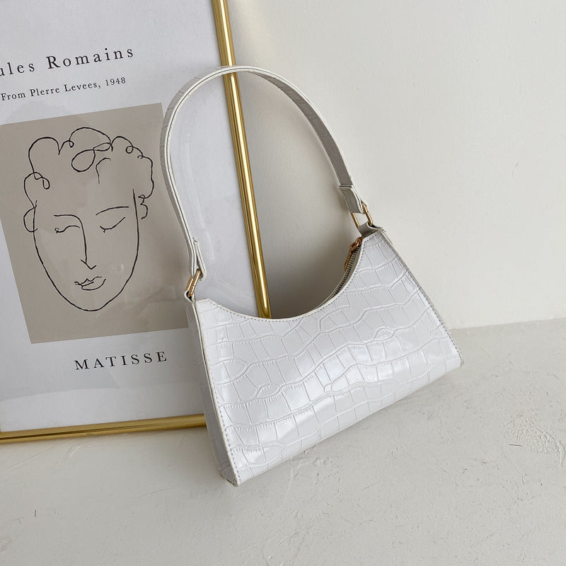 White handbag with gold accents on a light surface with a Matisse poster in the background