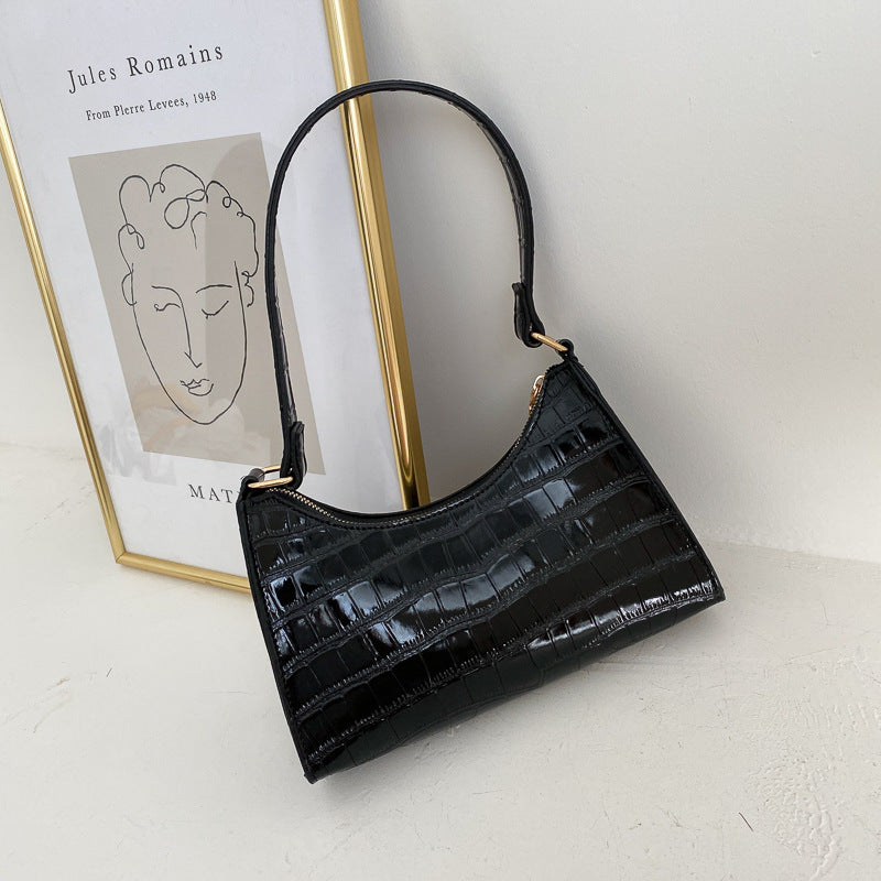 Black crocodile-patterned handbag on a light gray surface with a framed picture in the background.
