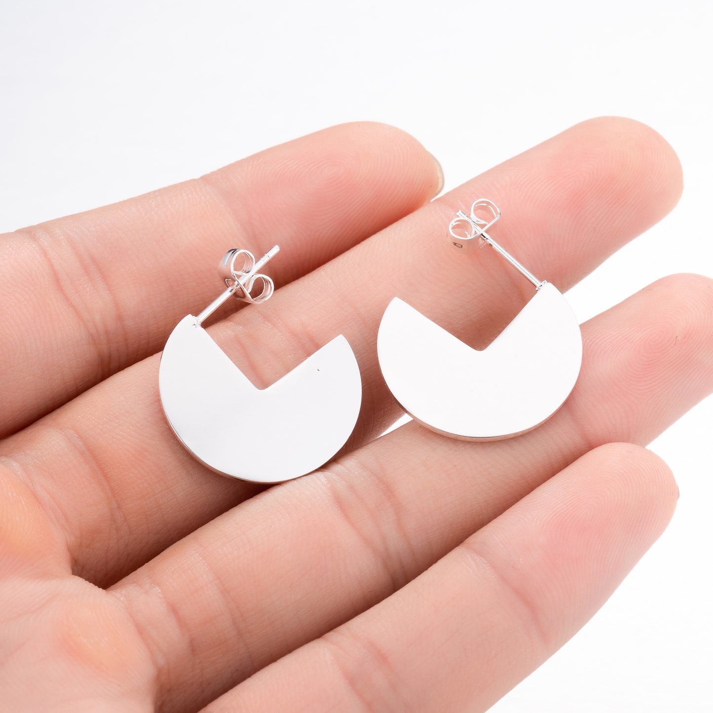 White half-circle earrings held between fingers on a white background
