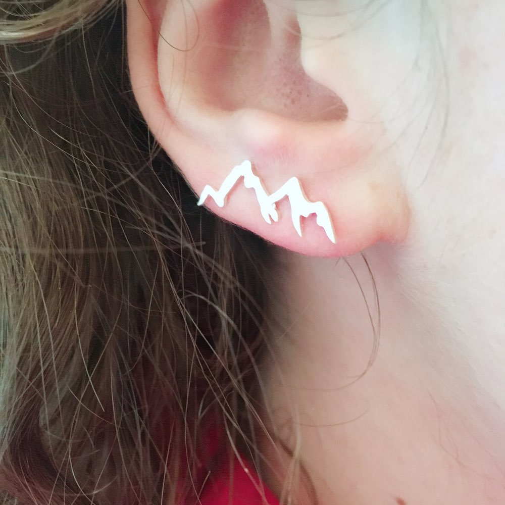 Close-up of an ear wearing a mountain-shaped earring with blurred background
