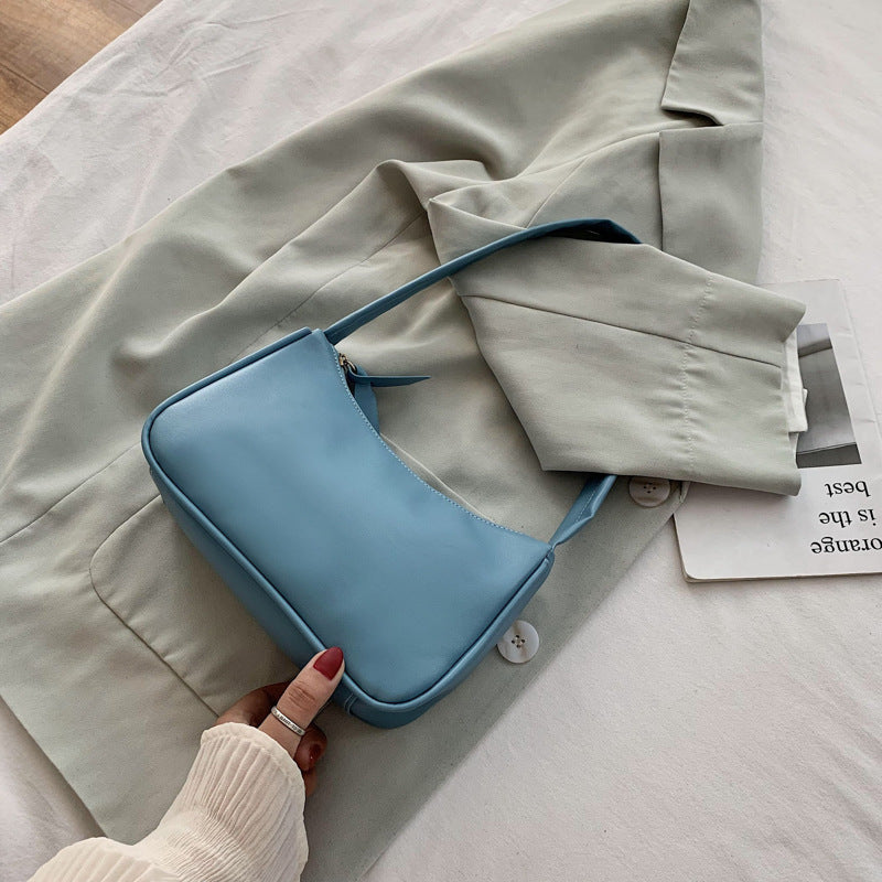 Blue handbag held by a hand on a light-colored fabric background