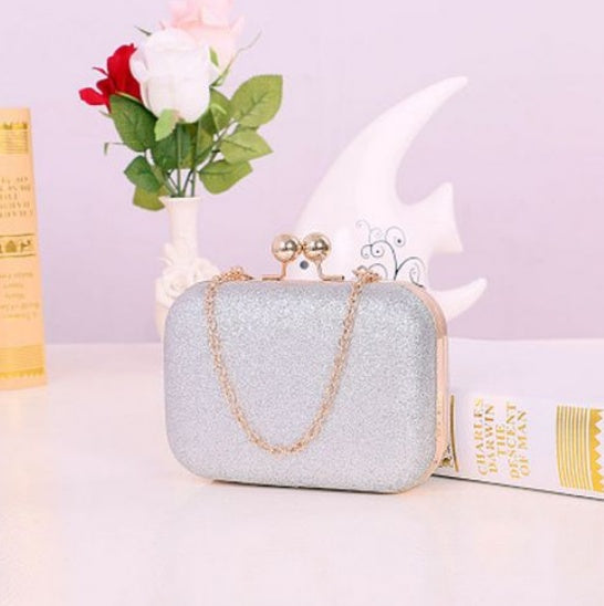 Silver glittery clutch bag with gold chain on a light purple background