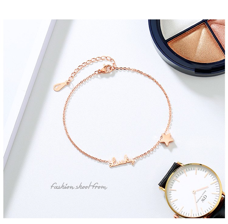 Rose gold bracelet with star charms on a white surface next to a watch.