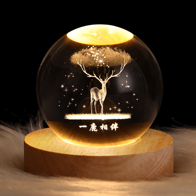 Decorative glass ball with a deer design on a wooden base against a dark background