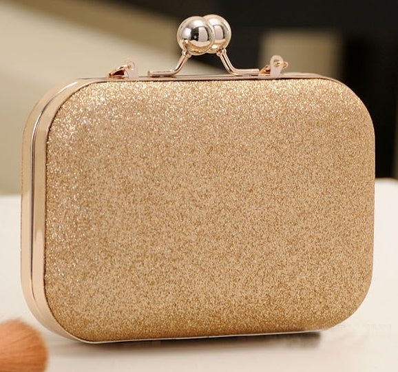 Gold glittery clutch bag with a decorative clasp on a neutral background