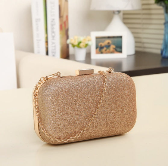 Gold glitter clutch bag on a light surface with a blurred indoor background