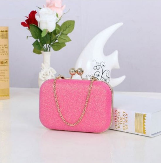 Pink clutch bag with gold chain on a white surface with decorative items.