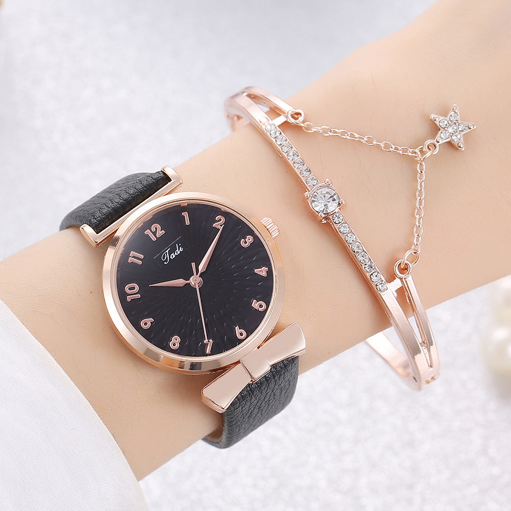 Wrist wearing a black watch with rose gold case and strap, paired with a star-shaped earring and bracelet on a light background.