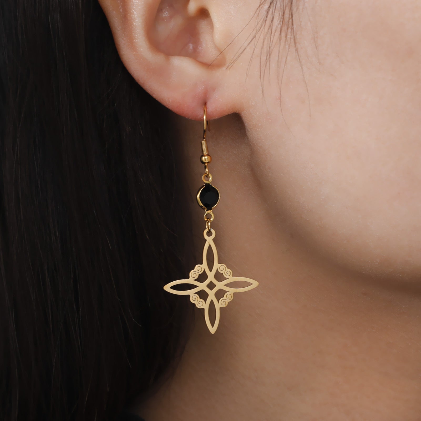 Gold earrings with a black bead worn by a person with dark hair.