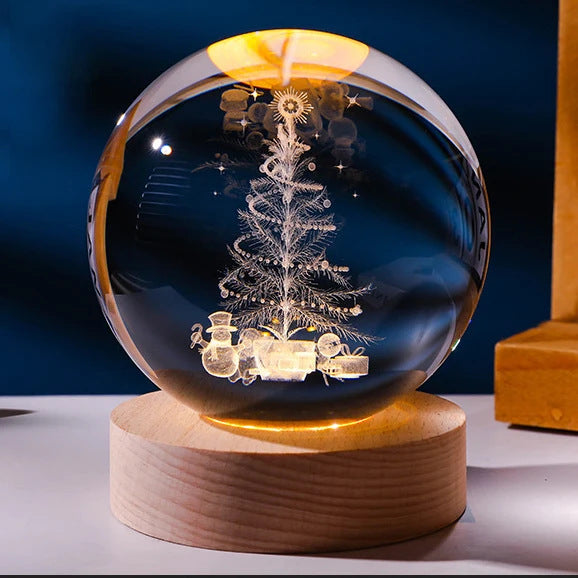 Crystal ball with Christmas tree and snowman design on a wooden base against a dark blue background