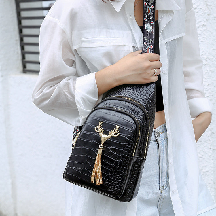 Person holding a black crocodile-patterned handbag with a gold tassel and deer emblem.