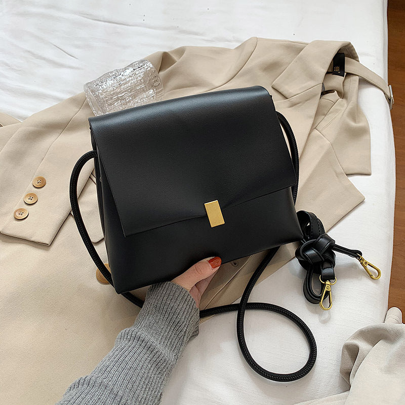 Black handbag with a gold clasp held by a person on a beige coat and white surface.