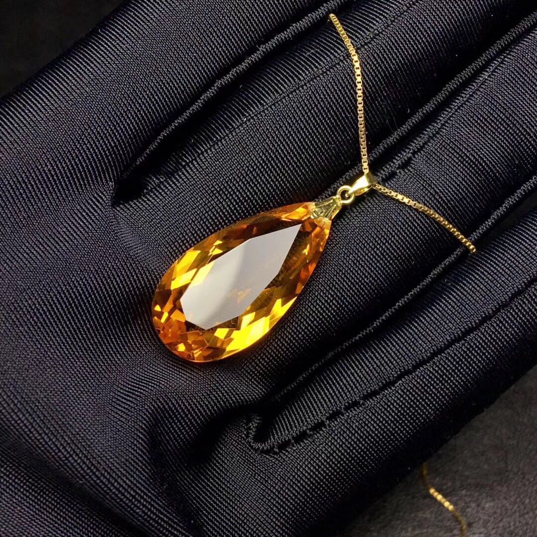 Gold necklace with a large orange teardrop pendant on a black fabric background