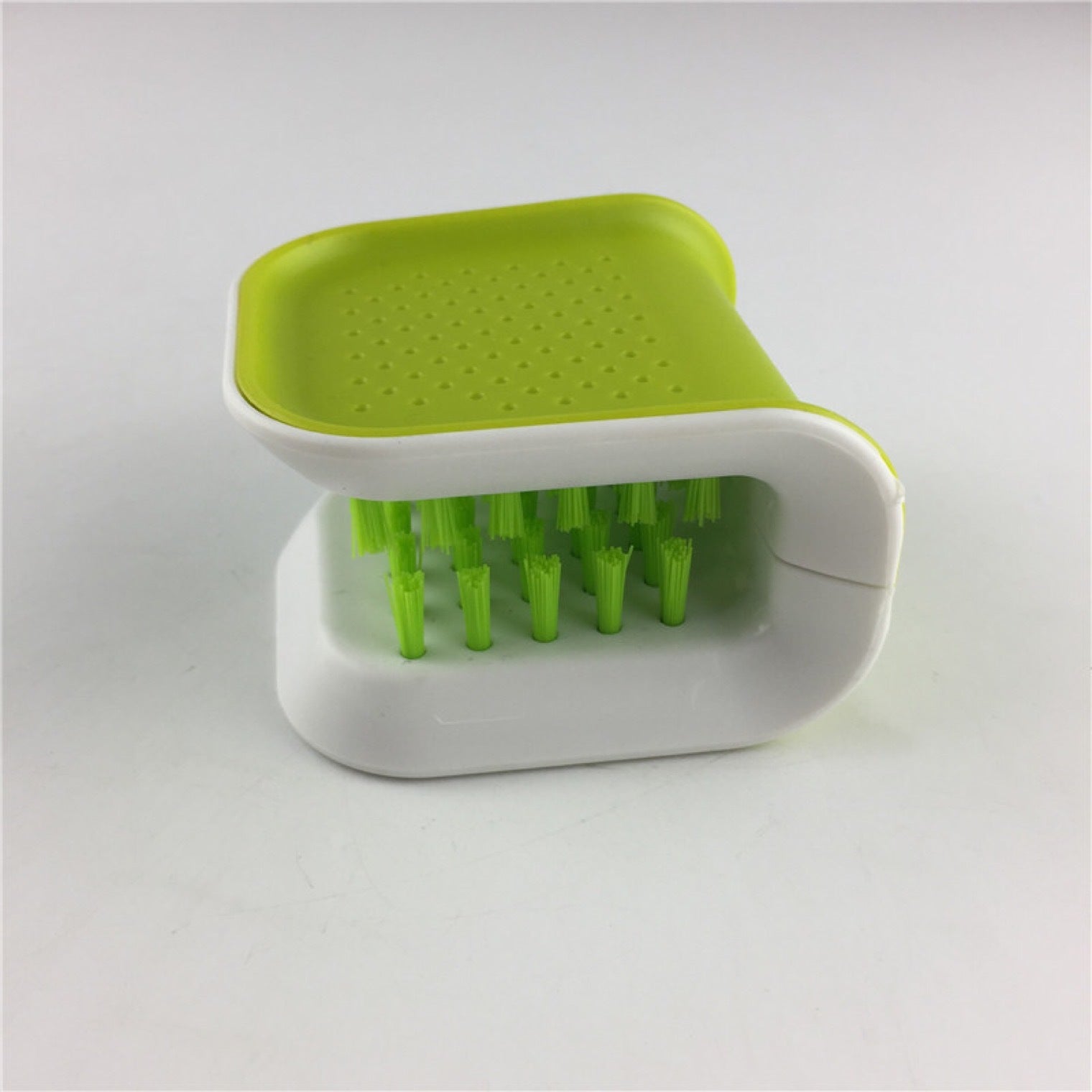 Green and white scrubber with a square head and bristle handle on a light gray background