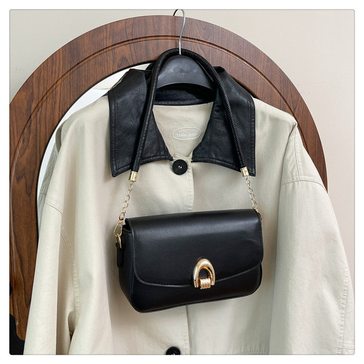 Black handbag with gold clasp hanging on a beige jacket against a wooden circular frame background