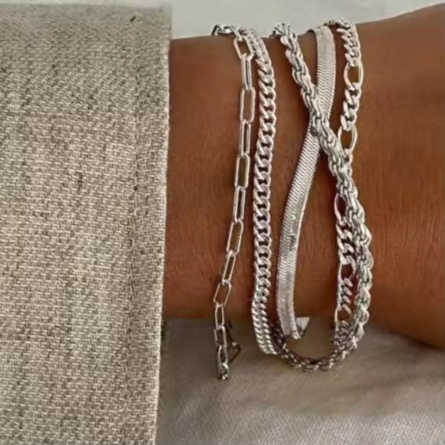 Three silver chain bracelets on a wrist against a neutral background