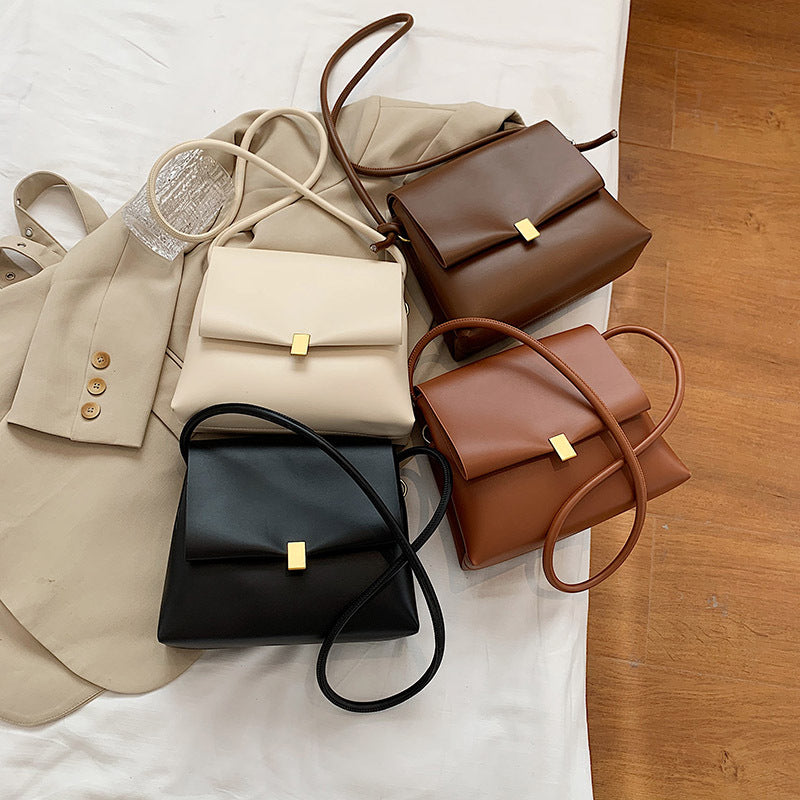 Four handbags in beige, brown, black, and brown with a gold clasp on a white surface.