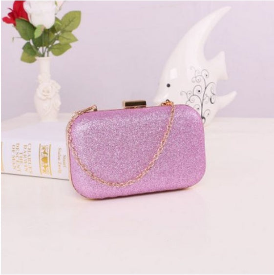 Pink glittery handbag with a gold chain on a light pink surface.