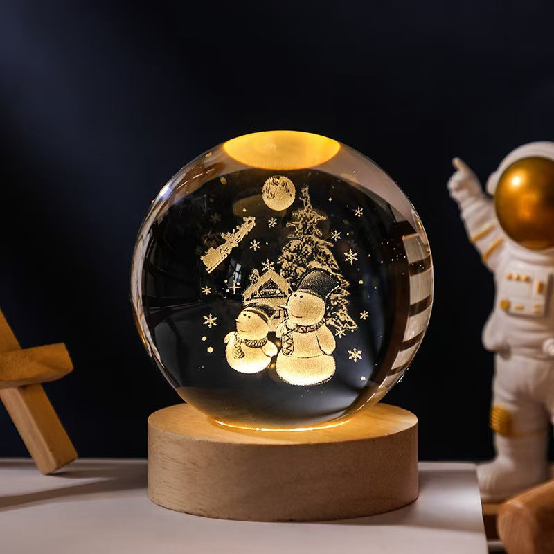 Decorative crystal ball with snowmen and a tree on a wooden base, with an astronaut figure in the background.