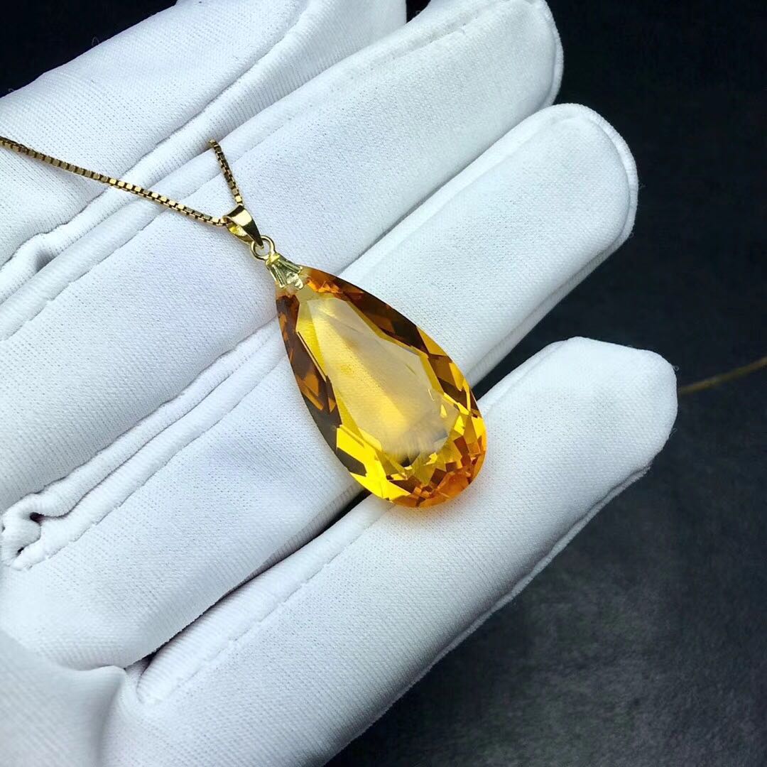 Yellow teardrop-shaped pendant on a white glove with a dark background