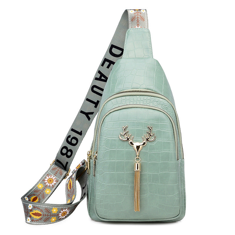 Mint green crossbody bag with deer emblem and floral strap on a white background
