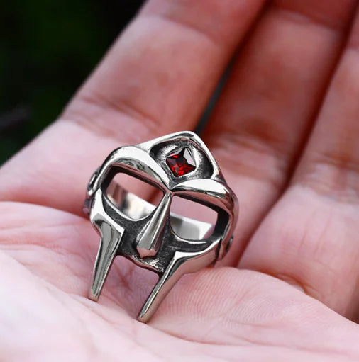 Silver mask-shaped ring with a red gemstone held in a hand.
