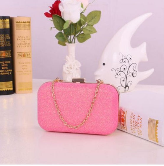 Pink clutch bag with gold chain on a surface with books and decorative items.